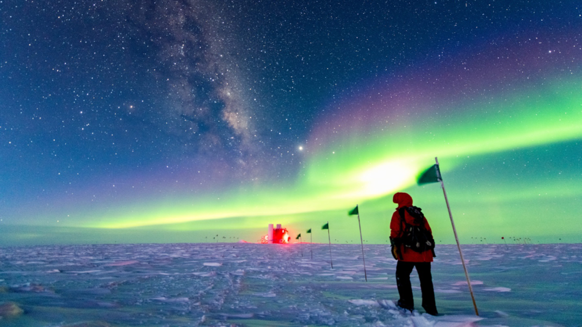 South Pole station under aurora with the IceCube neutrino telescope buried in the ice below.
